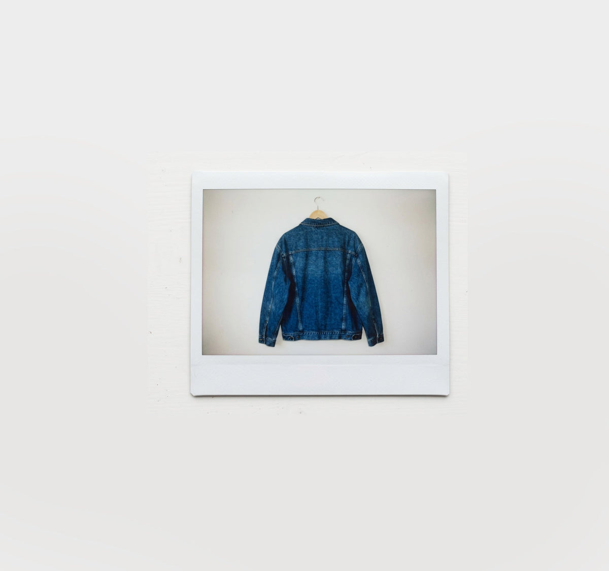 A polaroid of a wooden hanger with a dark denim jacket hanging on it