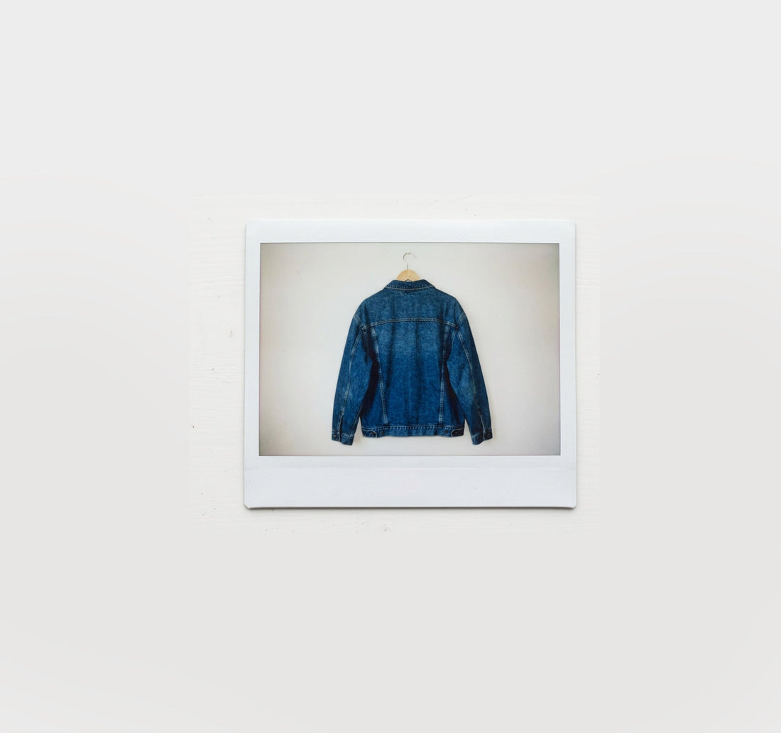 A polaroid of a wooden hanger with a dark denim jacket hanging on it
