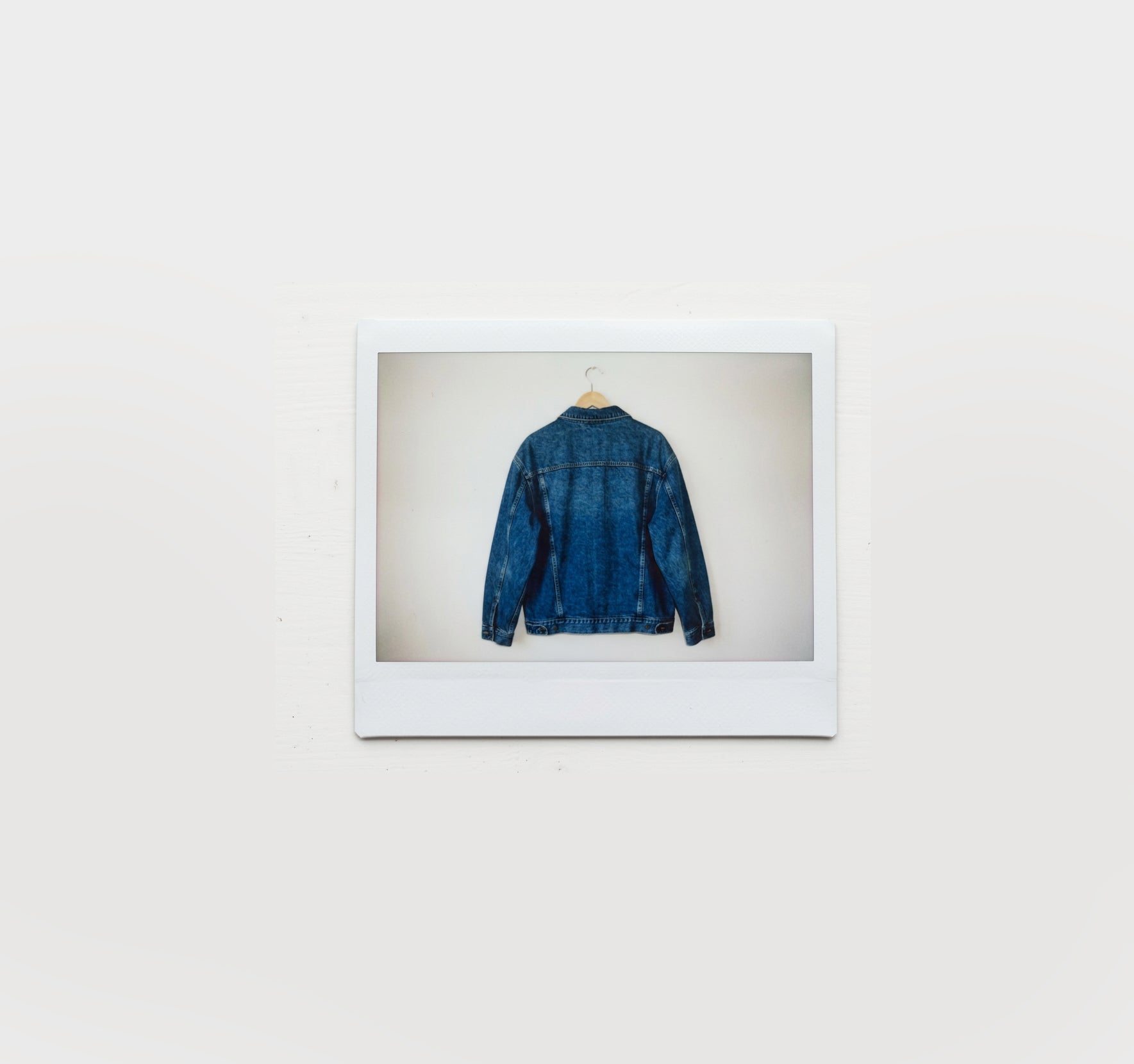 A polaroid of a wooden hanger with a dark denim jacket hanging on it